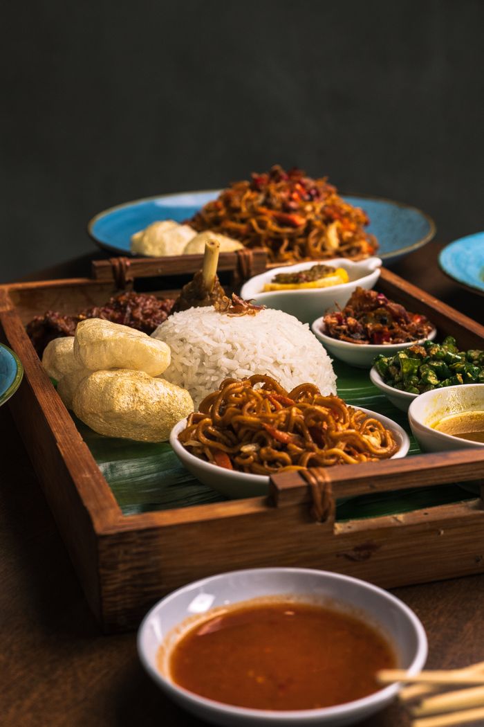 A vibrant Indonesian meal with rice, noodles, and various side dishes served in a wooden tray.